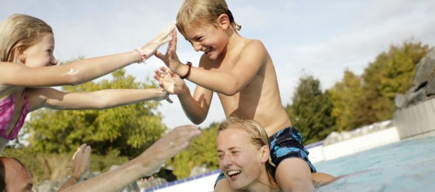 Vader, moeder en hun dochter en zoon hebben veel zwemplezier in het buitenbad van het Aqua Mundo zwembad van Center Parcs De Kempervennen.